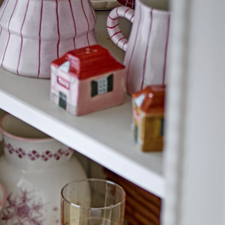 Homey House Stoneware Salt & Pepper Shakers, Set of 2, house-shaped with red tiled roofs, TOYS sign and shuttered windows, displayed on a shelf among pink striped jugs.