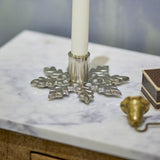 Kashi Snowflake Aluminium Christmas Candle Holder in silver, a low flat star-shaped base with leaf-patterned arms holding a white taper candle on a marble surface.