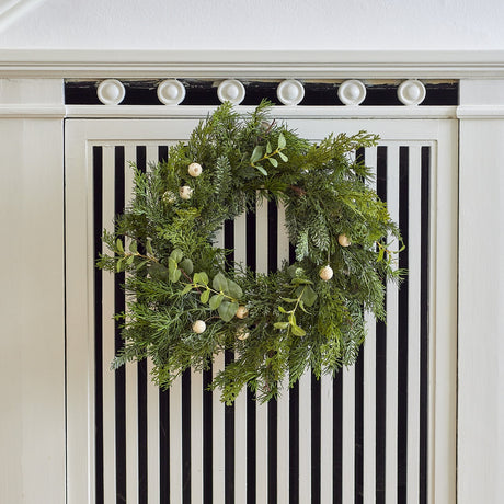Pine Artificial Christmas Wreath, 65cm, with mixed green foliage, soft eucalyptus sprigs and small round berries, hung on a white and black striped cabinet.