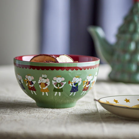 Peo Stoneware Christmas Bowl in green, 13cm, with a scalloped red rim and a band of angel mice illustrations, shown filled with pancakes beside a teapot and starred plate.
