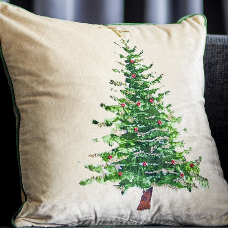 Evelin Cotton Christmas Cushion in cream, square velvet-look cushion with green piping and a printed Christmas tree decorated with beaded garlands, baubles and a star, shown on a sofa.