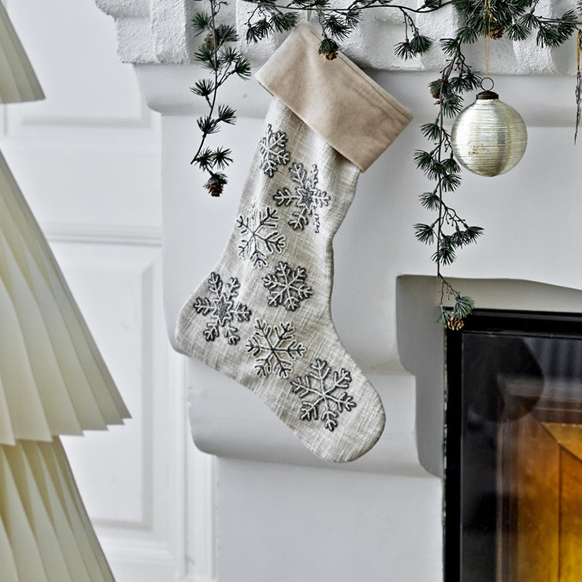 Ahsan Snowflake Cotton Christmas Decoration in beige, a woven fabric stocking with a folded cuff and beaded snowflake details, hanging from a mantelpiece.