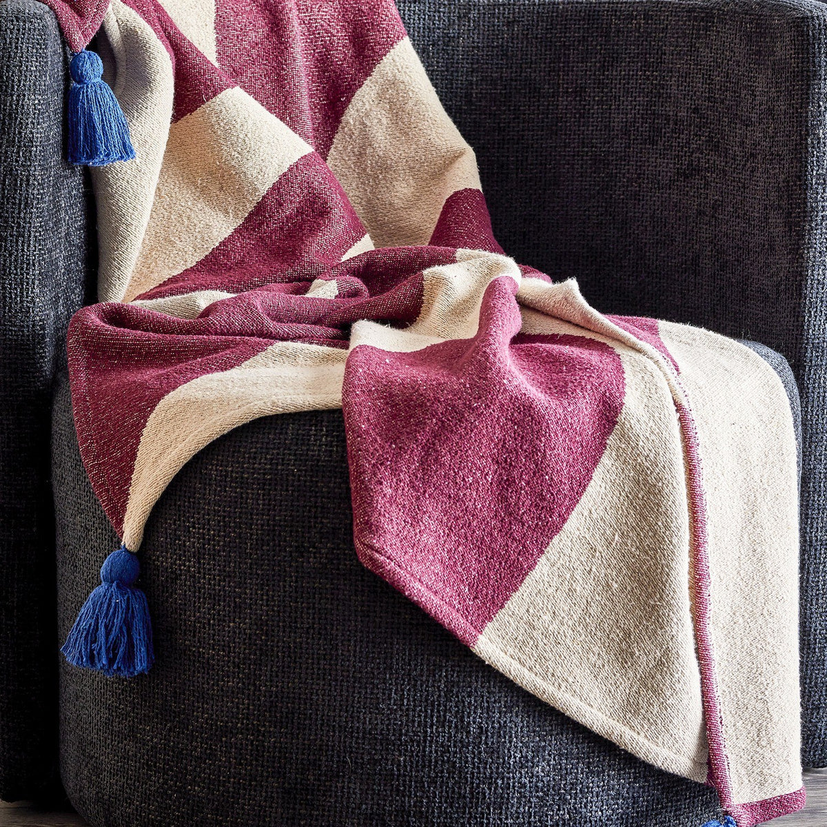 Cimmi Christmas Throw in burgundy and cream curved pattern with blue corner tassels, draped over a dark grey armchair.