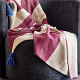 Cimmi Christmas Throw in burgundy and cream curved pattern with blue corner tassels, draped over a dark grey armchair.