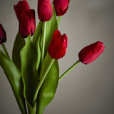 Tulip Artificial Bouquet in red, close-up of cupped tulip heads on long green stems with broad leaves, shown against a plain grey background.