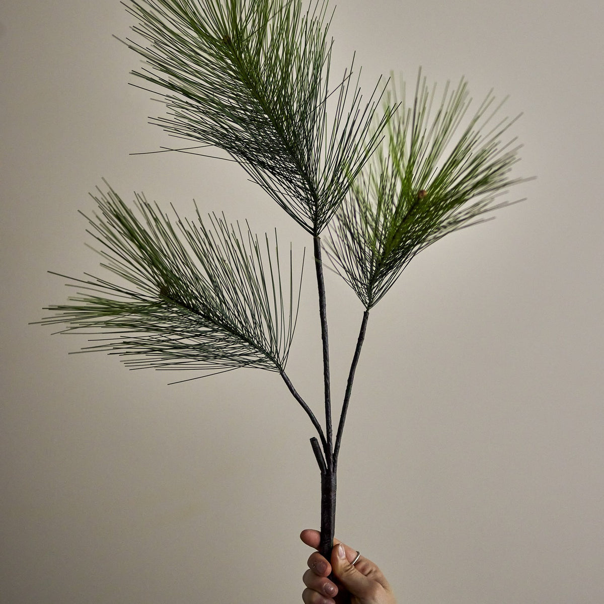 Pine Artificial Christmas Stem, 114cm, held by hand to show three branching green needle sprays on a slim bare stem against a plain neutral background.