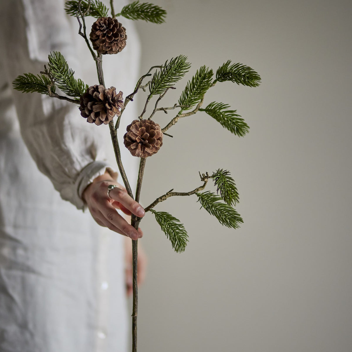 Artificial pine Christmas stem, 73x33cm, with green polyethylene needle sprays and three pinecones on a slim textured stem, held in hand against a neutral background.