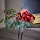 Rubia Artificial Christmas Bouquet in red, featuring large faux flowers, pine sprigs, pinecones and red berries, draped over a dark chair seat.