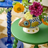 Nobu Fish Stoneware Vase in multicoloured hand-painted ceramic with blue dotted scales and fin, holding fresh flowers on a green side table beside a blue table.