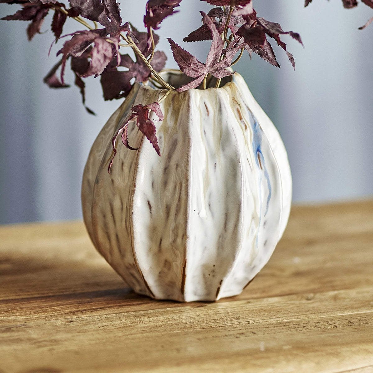Feray Wavy Stoneware Vase 18cm in White, ribbed form with an irregular rim and streaked glaze, holding dried foliage on a wooden surface.