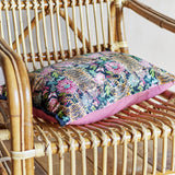 Lester Cotton Cushion in Multi, a rectangular lumbar cushion with a dense tiger and floral print in pink, navy, and green, shown on a rattan chair.