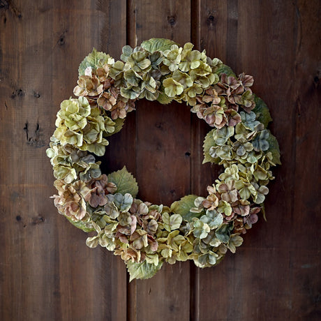 Hydrangea Artificial Wreath in multicoloured green, pink and tan tones, densely packed round faux blooms edged with serrated leaves, shown against a dark wood panelled background.