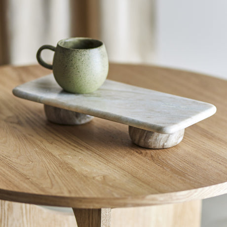 Fatin Marble Pedestal in beige, a rectangular polished marble slab on two rounded feet, shown on a wooden side table holding a green speckled mug.