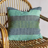 Isnel Green Striped Cushion in multicoloured woven stripes of teal, green, navy and cream, shown on a rattan chair.