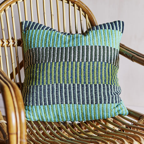 Isnel Green Striped Cushion in multicoloured woven stripes of teal, green, navy and cream, shown on a rattan chair.
