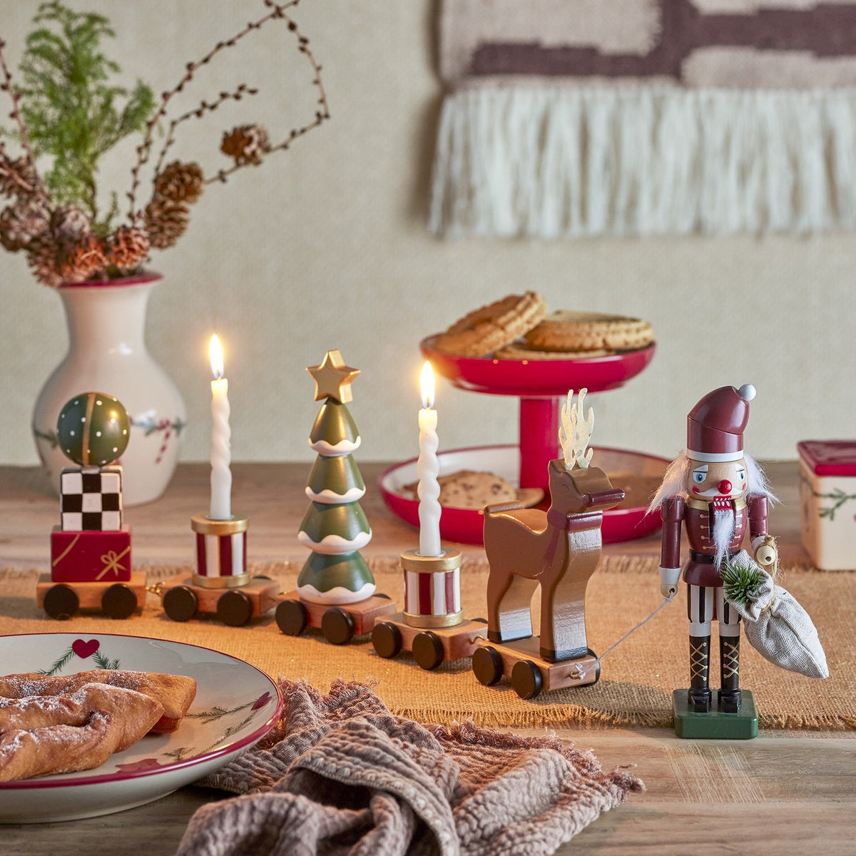 Vadim Christmas Decoration train with bauble, striped drum candle holders, tree and reindeer wagons, led by a wooden nutcracker figure on a festive table setting.