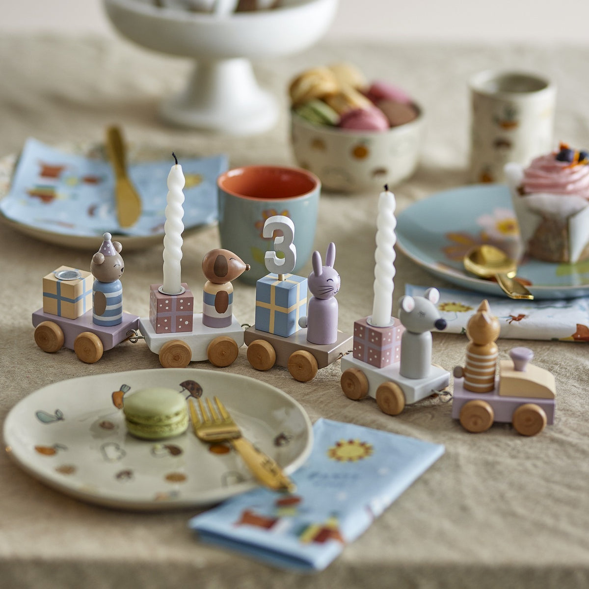 Junaid Cat Birthday Decoration wooden train with number 3 candle, mouse, rabbit and bear figures on parcel wagons, styled on a table with party tableware.