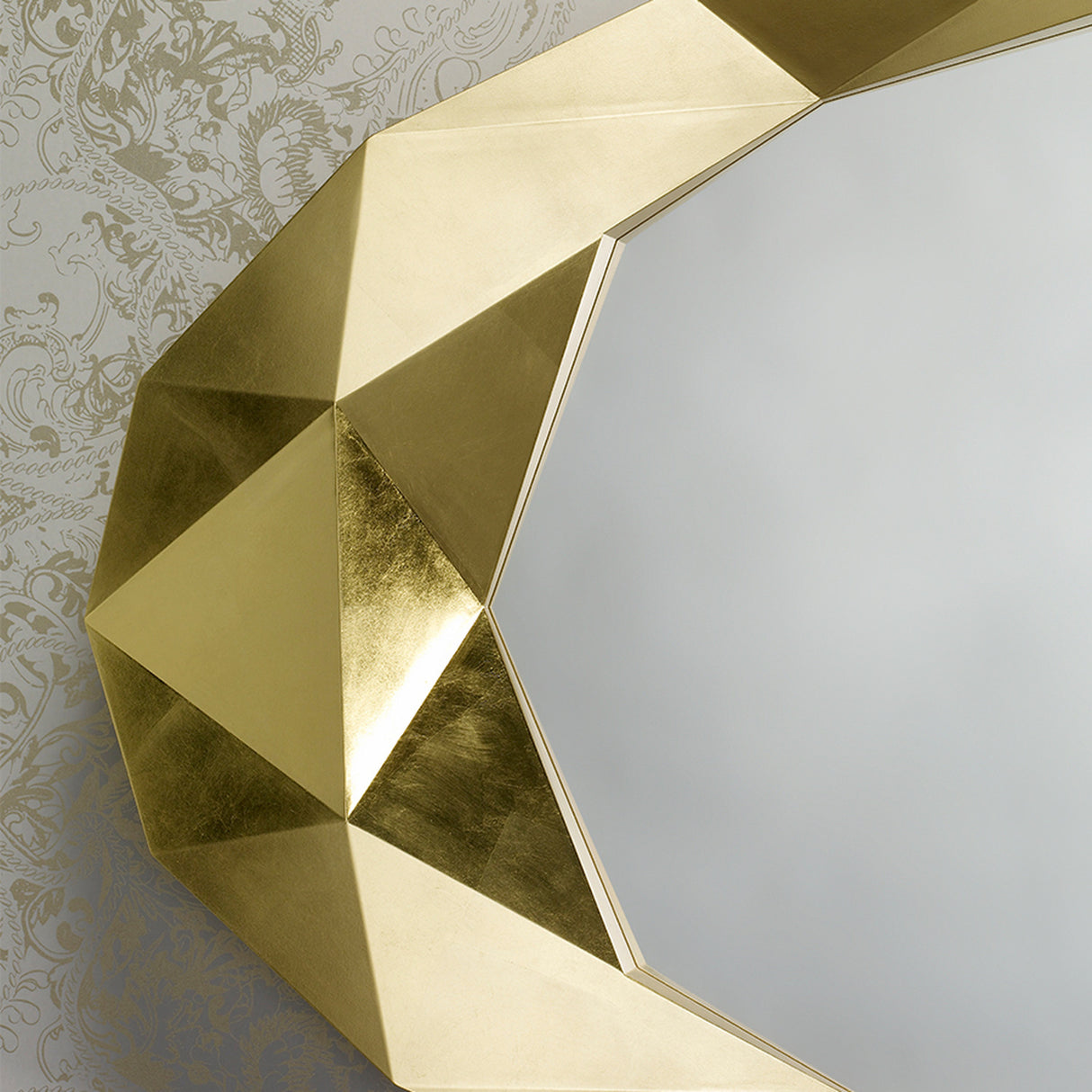 Close-up of the faceted gold leaf surround, each flat plane catching the light differently against damask wallpaper.