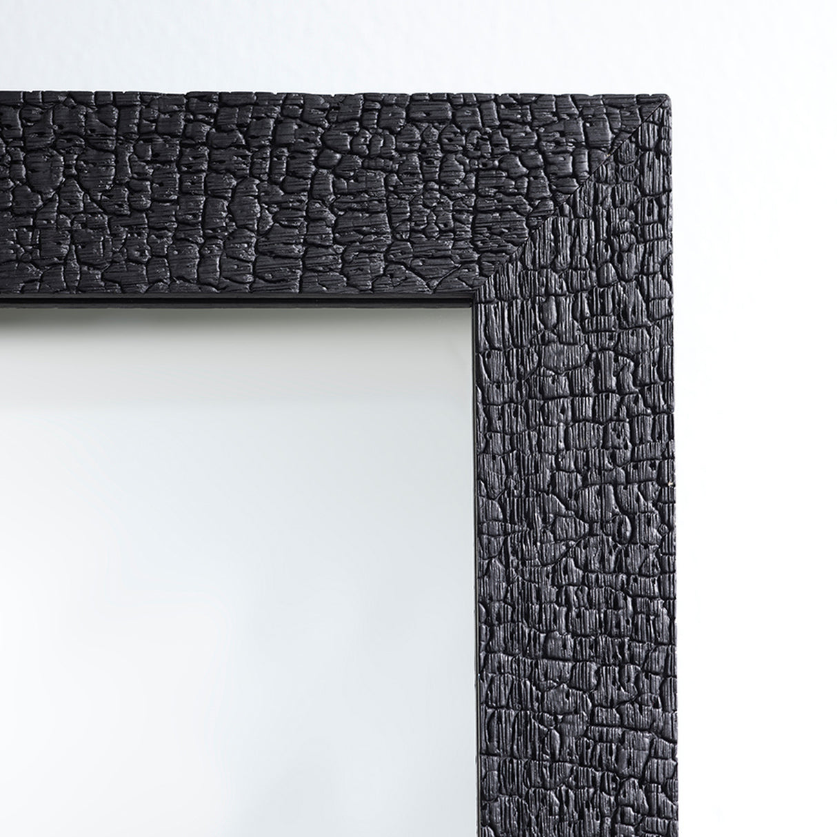 Close-up of the frame corner, the charred black timber broken into a fine crackled surface against the clear glass.