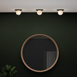 Halvessa LED Alabaster Downlight in black, three round ceiling fittings with glowing alabaster globes showing grey and brown veining, installed above a round wood-framed mirror on a dark green wall.