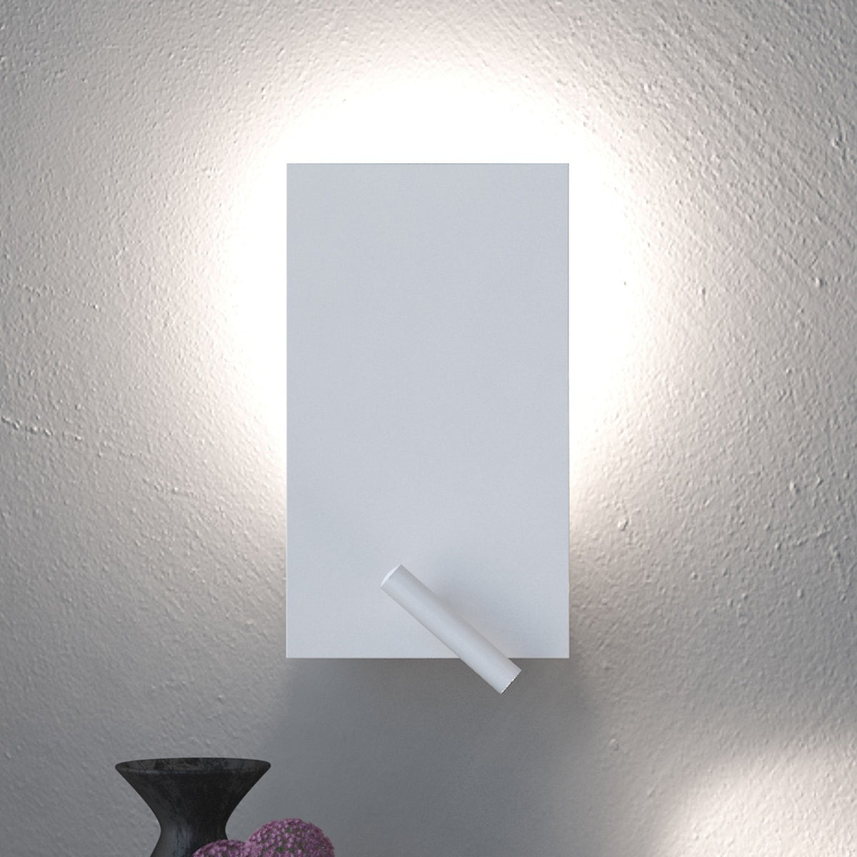 White iron flat twin switch wall light with reading light, rectangular plate casting a soft wall-wash glow and a slim integrated LED reading light at its lower corner, shown above a dark vase.