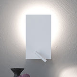 White iron flat twin switch wall light with reading light, rectangular plate casting a soft wall-wash glow and a slim integrated LED reading light at its lower corner, shown above a dark vase.
