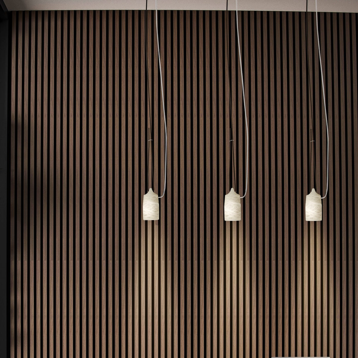 Paros Alabaster Pendant Light in white, three tapered alabaster shades with grey veining hanging at varied lengths against a striped wood wall.