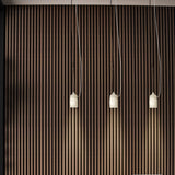 Paros Alabaster Pendant Light in white, three tapered alabaster shades with grey veining hanging at varied lengths against a striped wood wall.