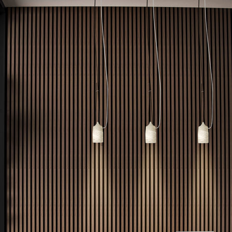Paros Alabaster Pendant Light in white, three tapered alabaster shades with grey veining hanging at varied lengths against a striped wood wall.