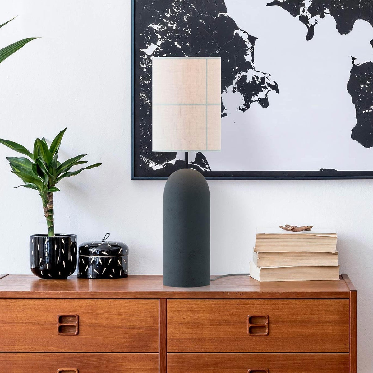 Rania table lamp with cylindrical anthracite concrete base and white cream fabric shade with stitched grid lines, styled on a wooden sideboard with books and a plant.