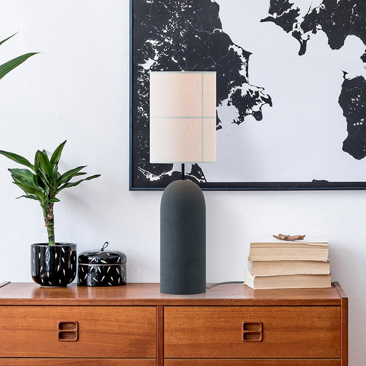 Rania Table Lamp with cylindrical anthracite concrete base and white cream fabric shade with stitched grid lines, shown on a sideboard in a living room setting.