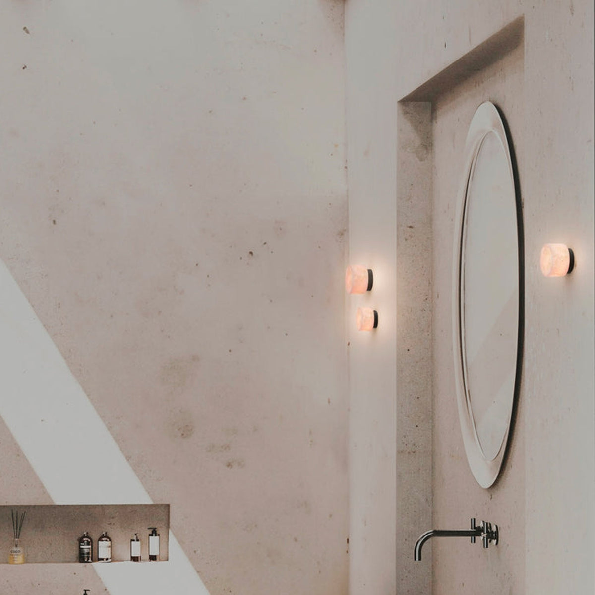 Rock LED Alabaster Drum Flush Wall Lights, IP44, with black aluminium base, mounted beside a round mirror in a bathroom setting.