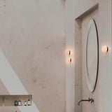 Rock LED Alabaster Drum Flush Wall Lights, IP44, with black aluminium base, mounted beside a round mirror in a bathroom setting.