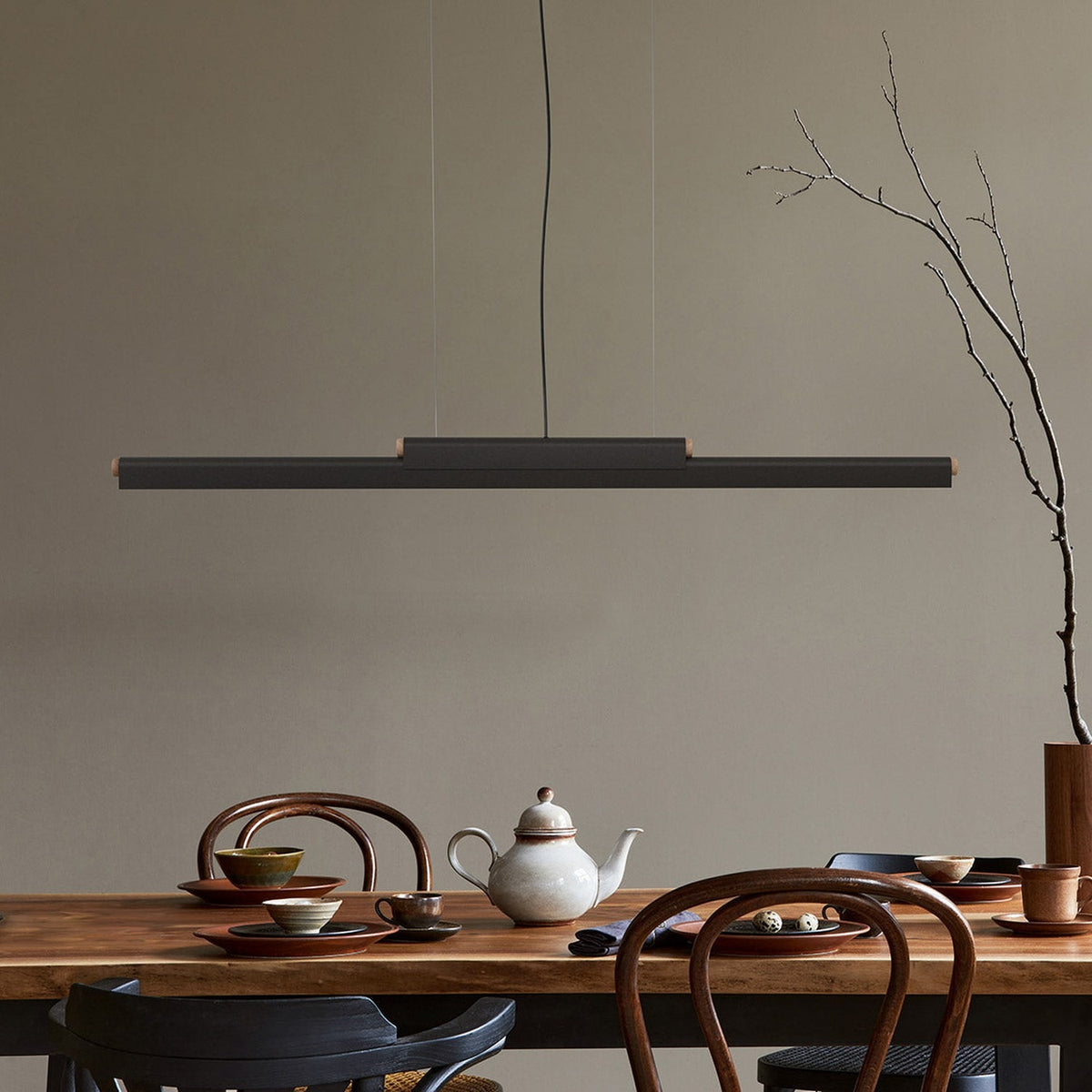 Rudi LED DALI Dimmable Linear Pendant Light in matt black with wood end caps, suspended above a wooden dining table set with ceramic tableware.