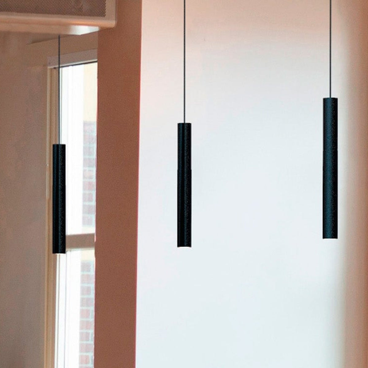 Rose Cylinder Pendant Light in matt black, slim cylinder shades on fine cables, shown in a room near a window and wall in varying lengths.