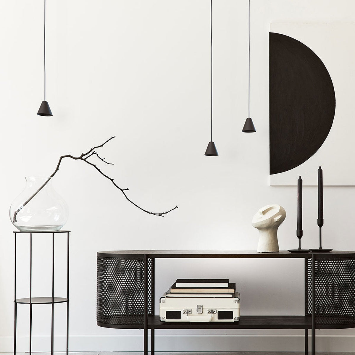 Rimini LED Cone pendant lights in matt black with conical iron shades, shown hanging at varying heights above a console table in a living room setting.