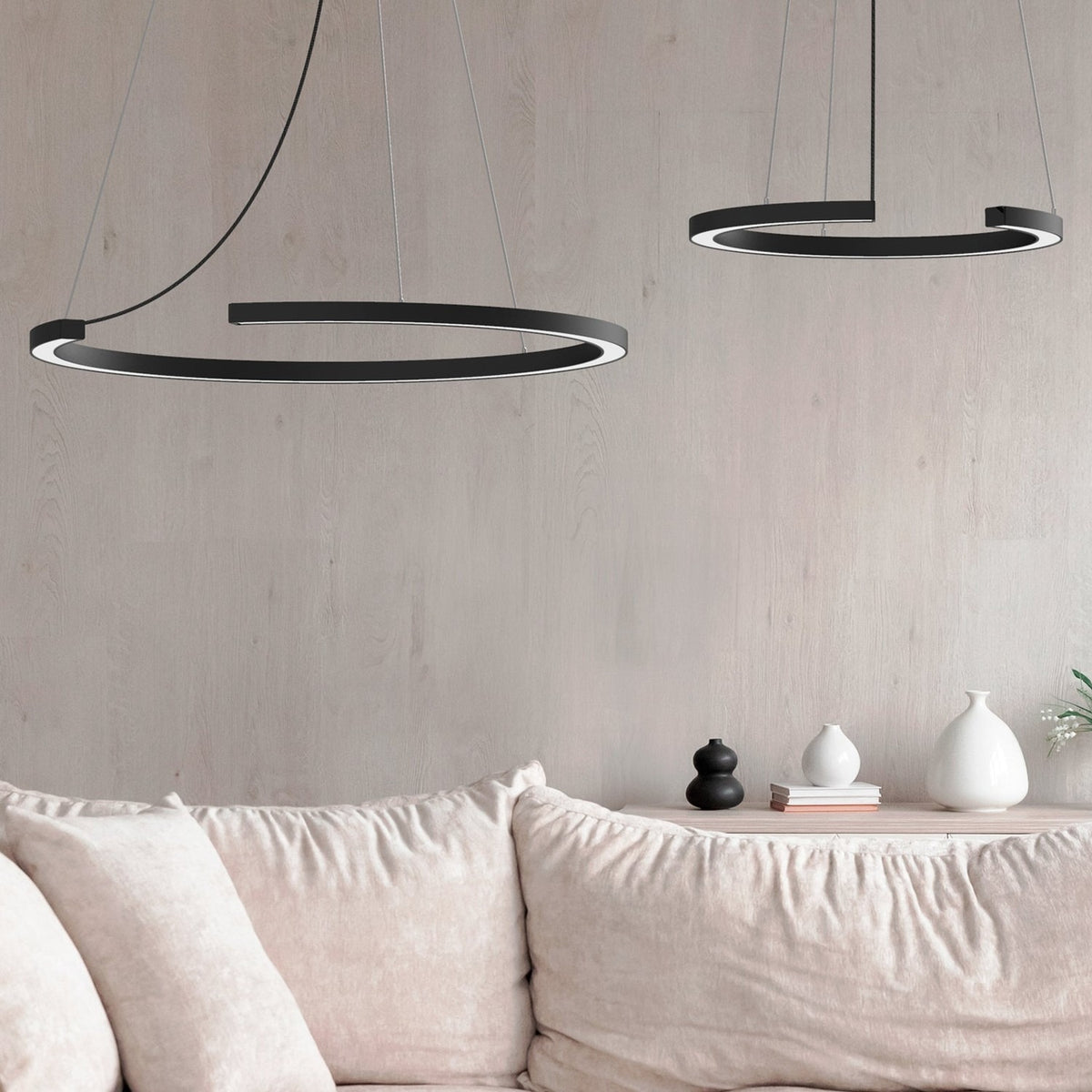Roberta LED DALI dimmable ring pendant lights in matt black aluminium, shown in two sizes above a beige sofa in a living room setting.