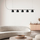Rio Linear 5 Light Dome Chandelier in matt black iron, five small dome shades along a slim horizontal bar, shown above a beige sofa and round coffee table.