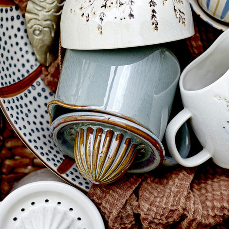 Pixie Stoneware Lemon Squeezer in green, showing the ribbed juicing dome fitted atop a handled jug, styled among ceramic tableware and linens.