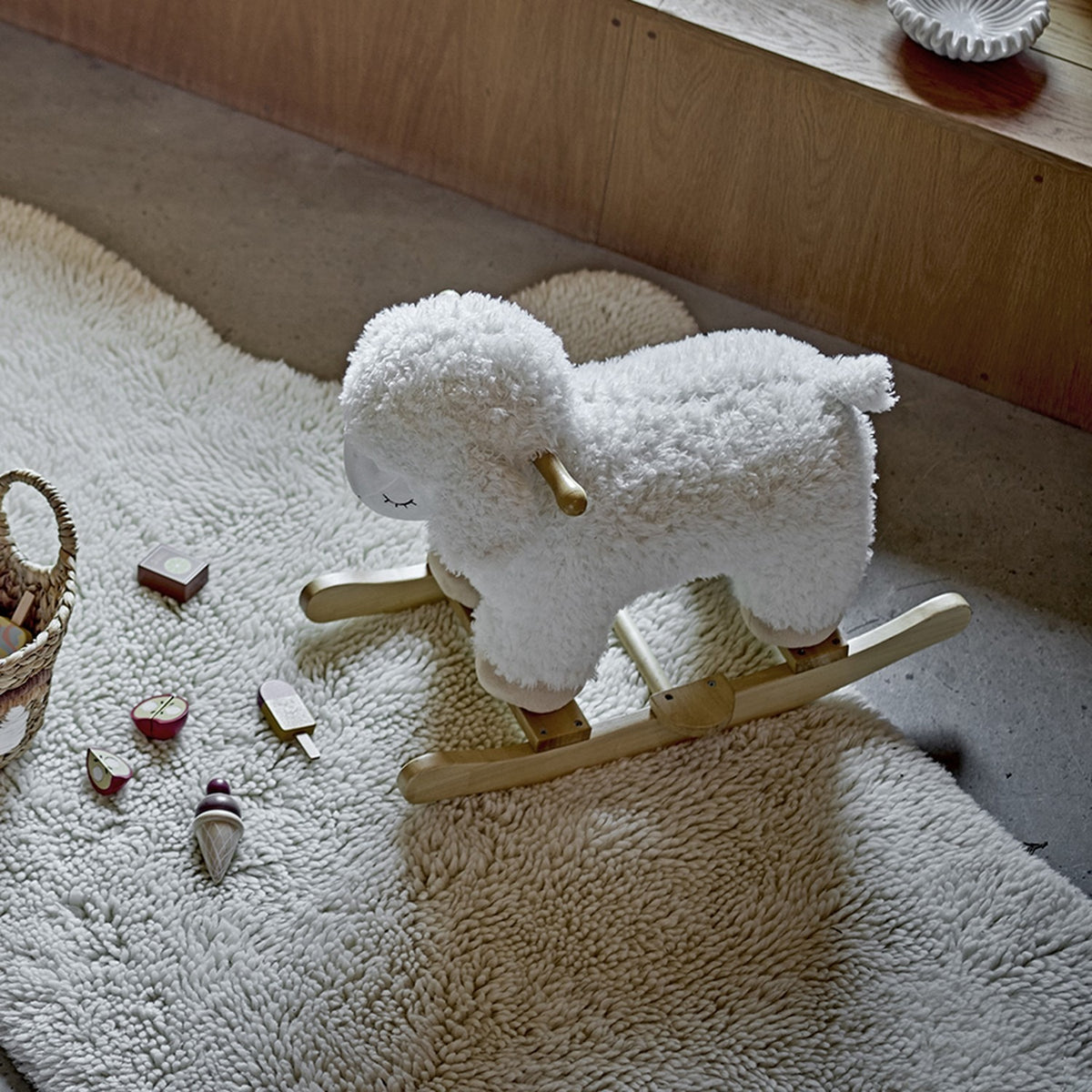 Laasrith Rocking Sheep in white, a curly fabric ride-on toy with wooden handle and curved poplar rockers, shown on a textured rug in a nursery setting.