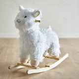 Kinto Rocking Llama in white, a shaggy fabric ride-on toy with embroidered face, wooden handle grip, and curved wooden rockers, shown on a light wood floor.