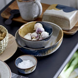 Jules Crackle Stoneware Bowl 17.5cm in blue and grey reactive glaze, shown filled with garlic bulbs alongside matching plates and a smaller bowl on a dark table.