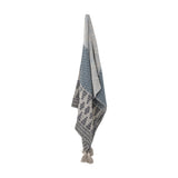 Milas Cotton Throw in blue, hanging against a plain white background, showing woven zigzag, striped, and diamond-motif bands with tasselled corners.