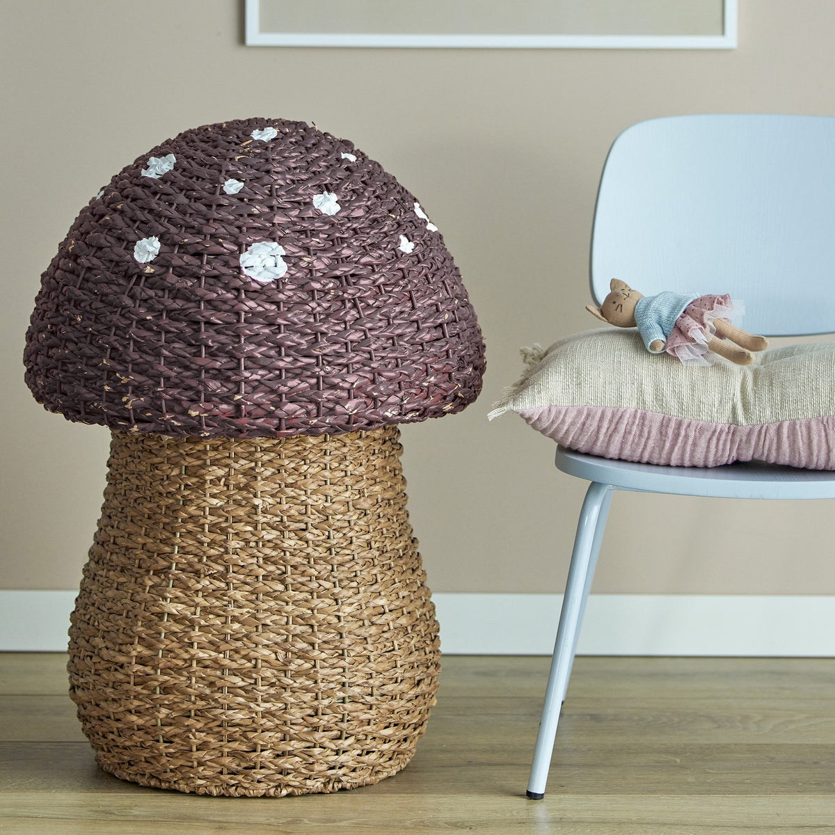 Corintha Mushroom Seagrass Basket with Lid in brown, woven stem storage with domed spotted cap, shown beside a light blue chair in a nursery setting.