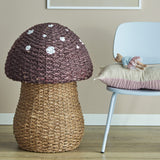 Corintha Mushroom Seagrass Basket with Lid in brown, woven stem storage with domed spotted cap, shown beside a light blue chair in a nursery setting.