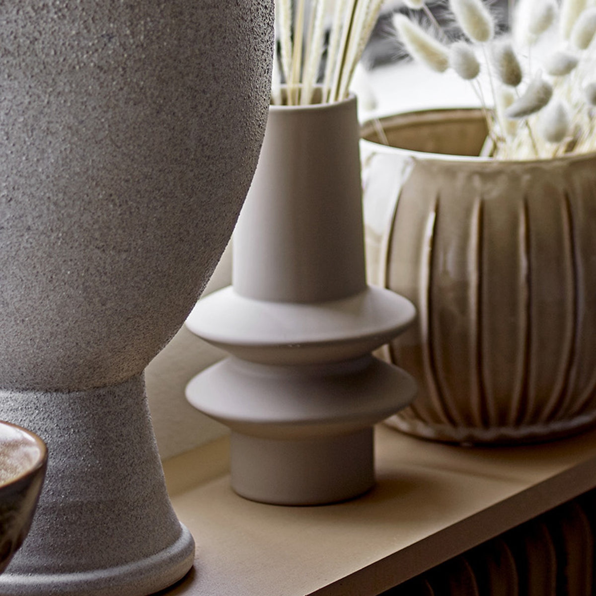 Isold Stoneware Vase 22cm in beige with a slender neck and two stacked flared rings on a short foot, matt ceramic finish, shown among other vases.