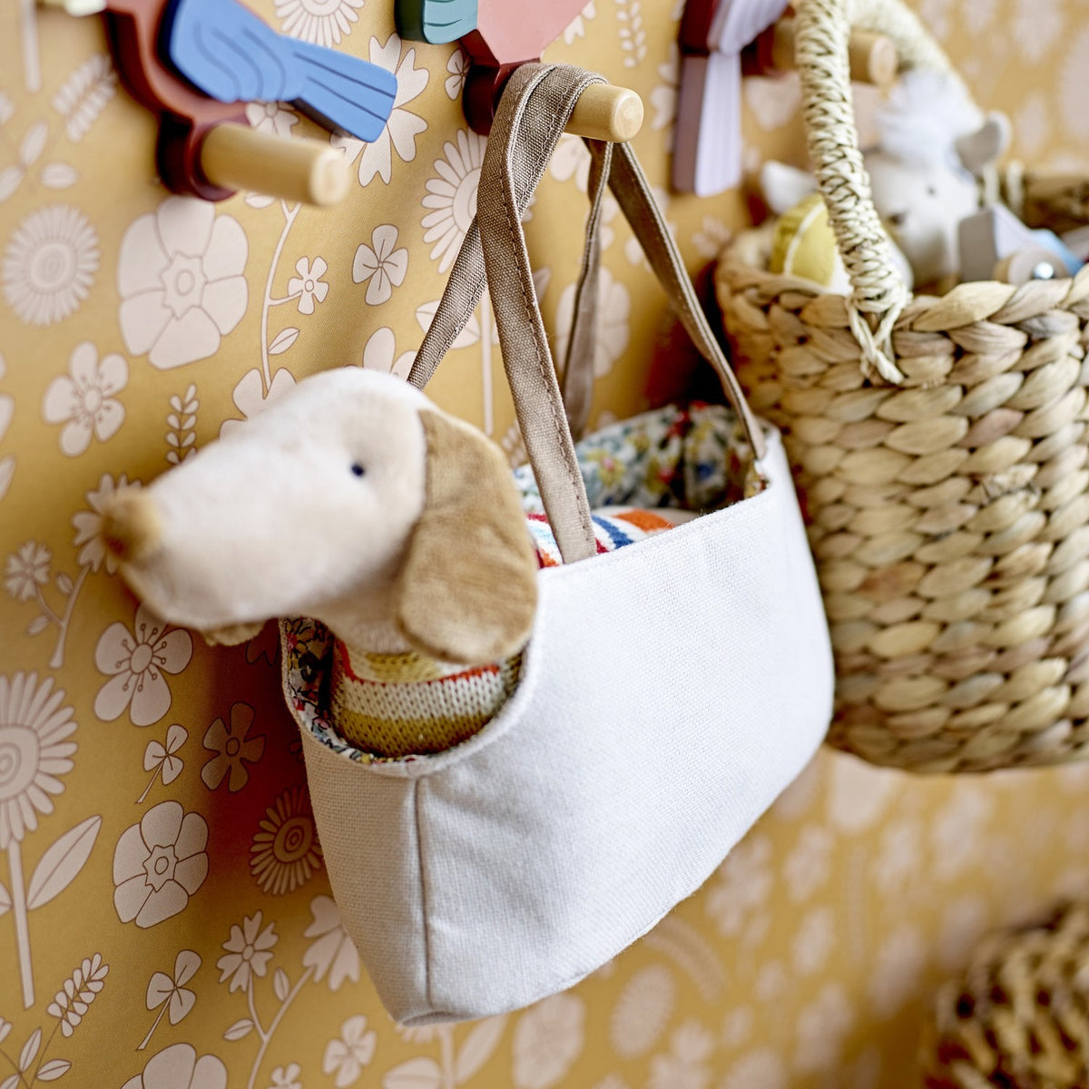 Hilena Soft Toys Set of 2 - plush sausage dog in striped knit jumper peeking from a white fabric tote with floral lining, hung on wall hooks.