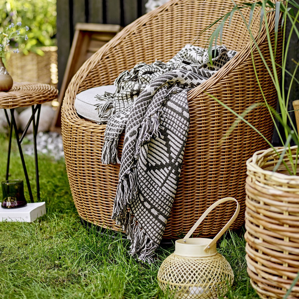 Gutte Geometric Throw in black and white, woven with diamonds and checks, fringed ends, draped over a wicker chair in an outdoor garden setting.