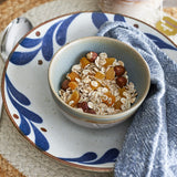 Camellia Porcelain Deep Plate 22cm in blue with sweeping leaf brushstrokes, holding a smaller matching bowl filled with muesli, hazelnuts and dried apricots.