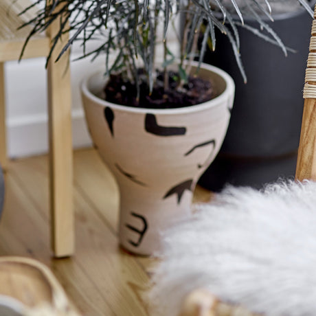 Nans Terracotta Vase 27cm in natural, footed cup shape with flared bowl and slim stem, painted black shapes and dots, planted with greenery in a living room setting.